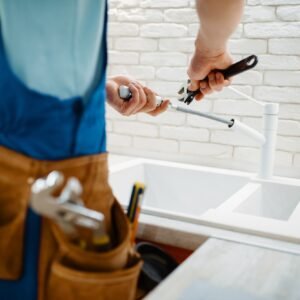 Plumber in uniform fixing faucet in the kitchen